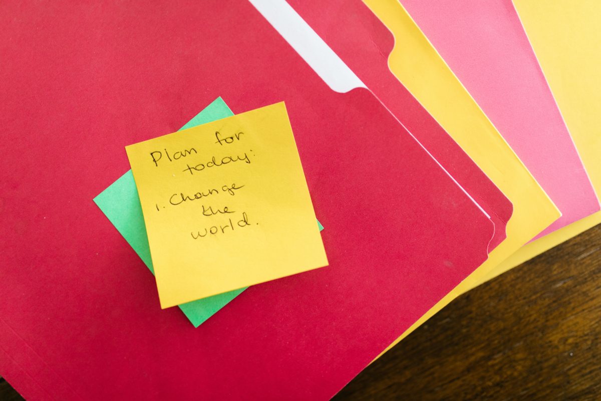 A stack of colored photos is fanned out, with a Post-It note on the top that reads, Plan for Today: Change the world